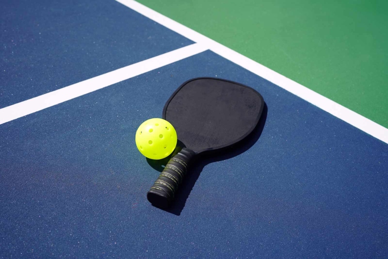 A yellow wiffle ball and paddle lying on a blue and green court