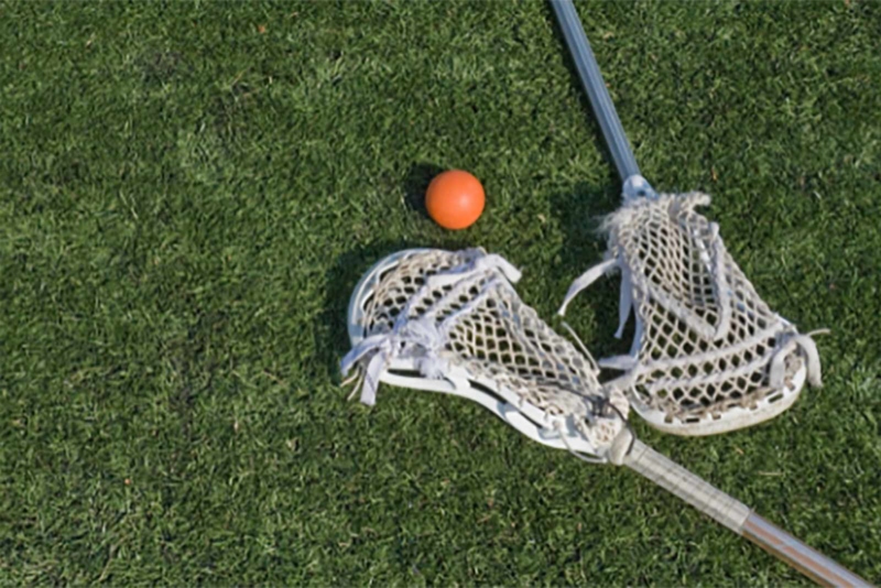 Two lacrosse sticks and an orange ball laying on green turf